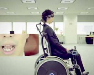 スーツ姿の男性が筋電位車いすに乗っている。真横からのアングル